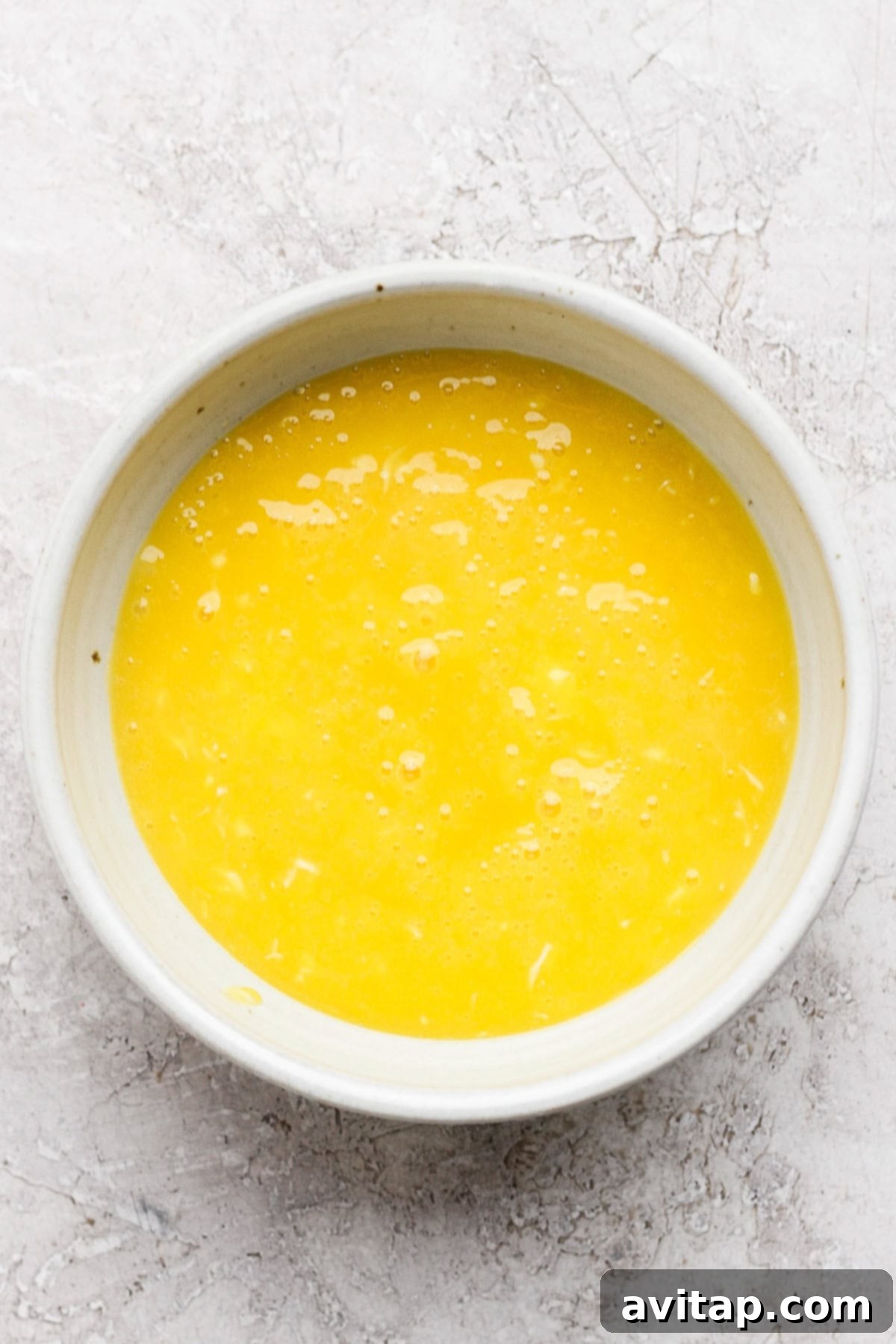 A white bowl filled with beaten eggs on a textured white surface.