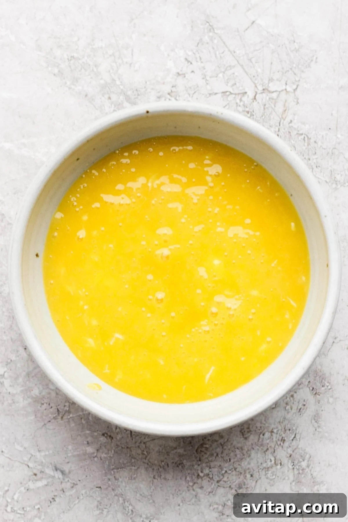 Golden Honey Lemon Curd 4 A pristine white bowl filled with perfectly beaten eggs, ready for the next step in creating a luscious lemon curd, resting on a clean, textured white surface.