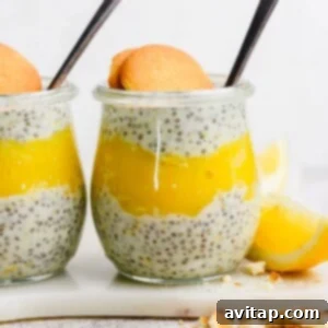 Golden Honey Lemon Curd 5 A glass jar filled with layered chia pudding and vibrant yellow lemon curd, topped with a round cookie and accompanied by a spoon and a fresh lemon wedge.