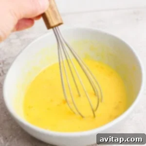 A hand whisking yellow batter in a gray bowl.