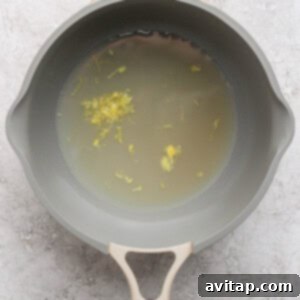 A gray saucepan filled with water and small yellow floral bits on a textured light gray surface.