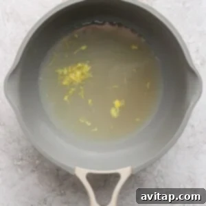 A gray saucepan filled with water and small yellow floral bits on a textured light gray surface.