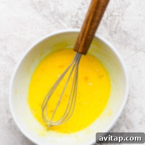 A whisk being used to combine the tempered eggs with the hot lemon mixture in a saucepan, showing the thickening process of the lemon curd.