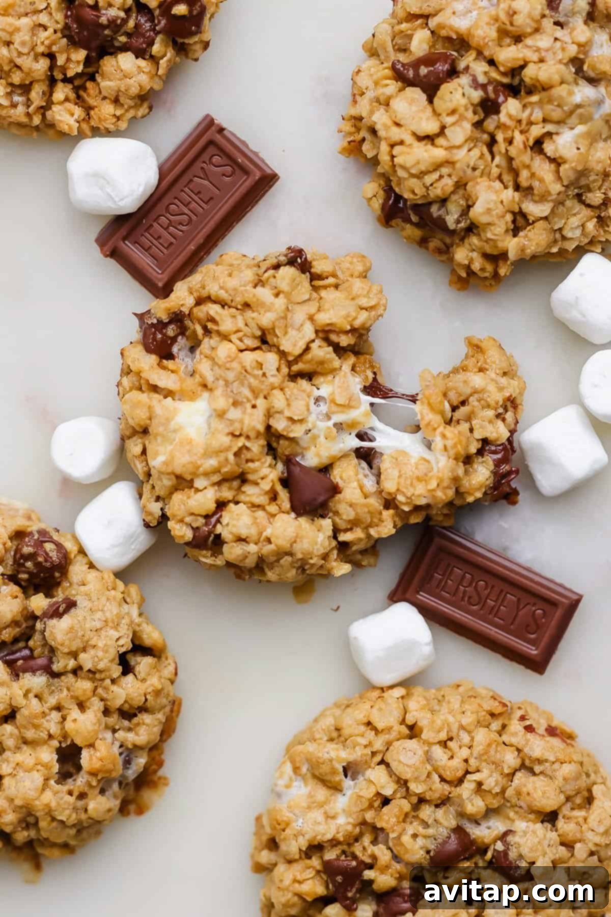 Delicious oatmeal cookies with chocolate chips and melted marshmallows, elegantly arranged with extra mini marshmallows and chocolate chunks on a stylish marble surface.