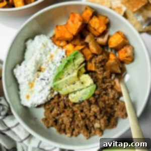 A bowl containing ground beef, roasted sweet potatoes, cottage cheese with hot sauce, and avocado slices, topped with black pepper.