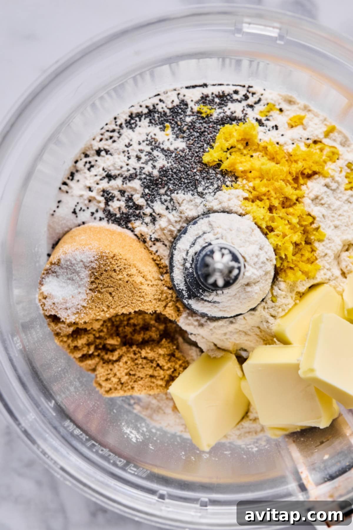 A food processor bowl containing flour, brown sugar, poppy seeds, lemon zest, salt, and cubes of butter, ready to be mixed for the fruit pizza crust.