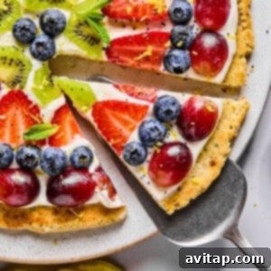 A slice of fruit pizza topped with blueberries, strawberries, grapes, kiwi, mint leaves, and lemon zest on a cookie crust with cream cheese frosting.