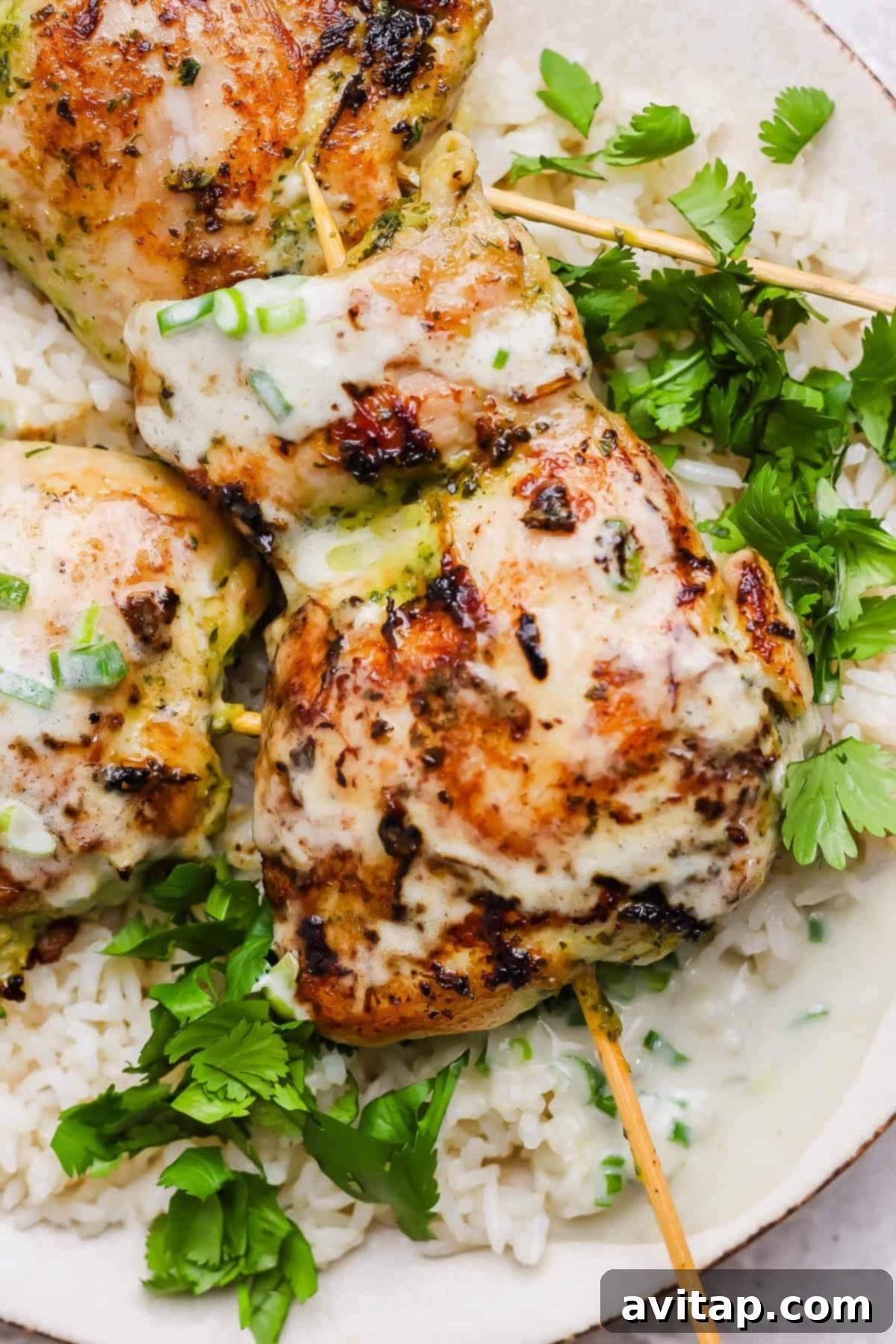 Grilled green curry chicken skewers with creamy coconut sauce, served over white rice and garnished with fresh cilantro.