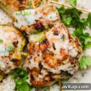 Close-up of grilled chicken skewers with creamy sauce, served on white rice and garnished with fresh cilantro and chopped green onions.