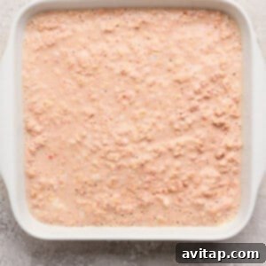 Strawberry Cheesecake Oat Bake 10 A white rectangular baking dish filled with an uncooked, vibrant pinkish oatmeal mixture, ready for baking, set on a textured, light-colored surface.