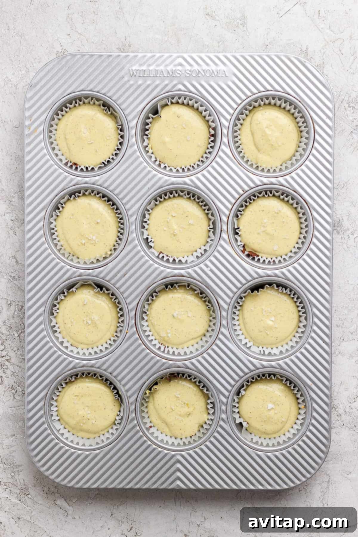 A metal muffin tin filled with twelve paper liners, each containing the finished pistachio cheesecake batter before freezing.