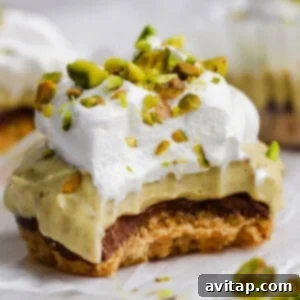 A dessert bar with a crumbly base, chocolate layer, creamy filling, whipped topping, and chopped pistachios, with a bite taken out of it.