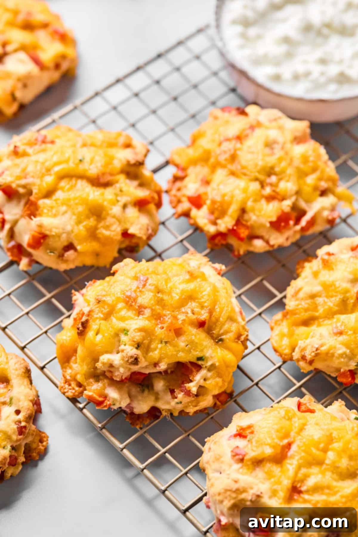 Freshly baked cheddar and red pepper savory biscuits cooling on a wire rack, with a bowl of creamy cottage cheese in the background, hinting at the star ingredient.