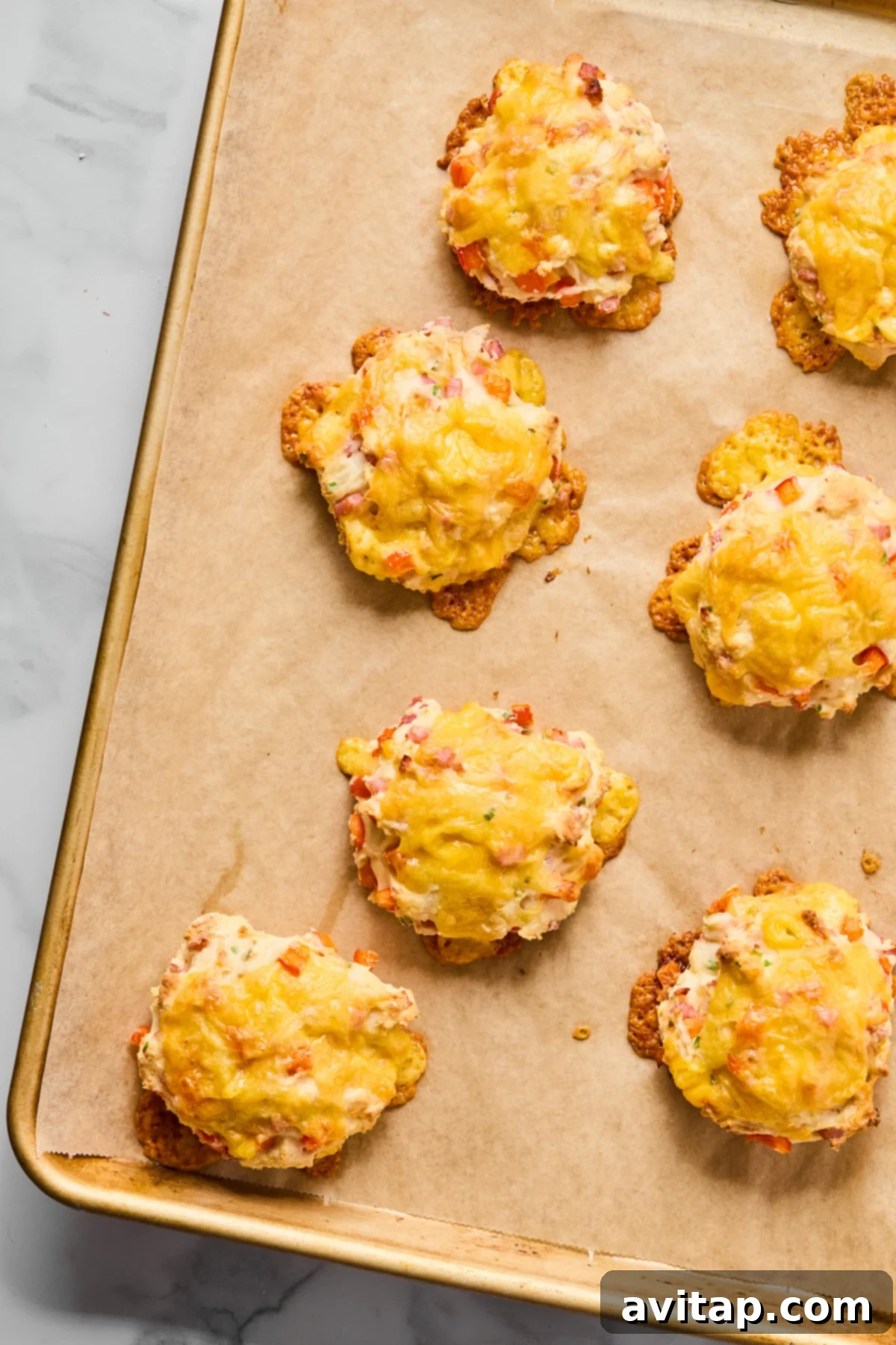 A baking sheet, thoughtfully lined with parchment paper, presents a row of seven perfectly baked savory cheese and vegetable biscuits, golden and inviting.