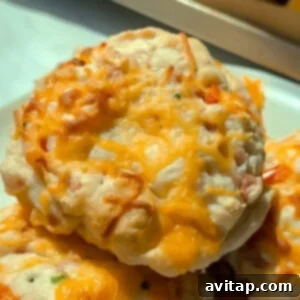 A close-up of cheesy baked biscuits with melted cheddar cheese on top, served on a white plate, highlighting their appetizing texture and golden crust.