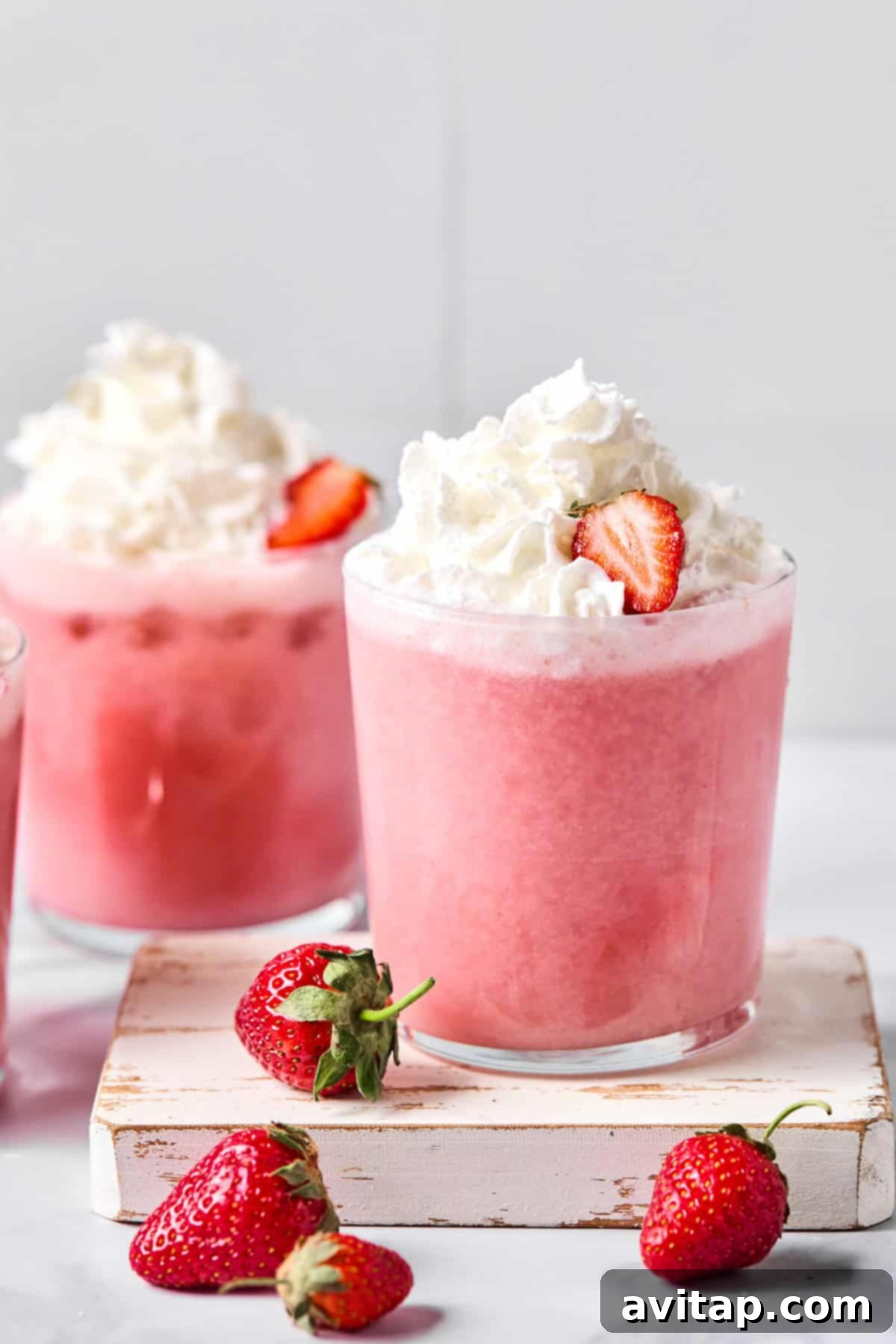 Quick Strawberry Dream Cocktail 5 A glass of pink strawberry smoothie topped with whipped cream and a strawberry slice, with fresh strawberries placed beside the glass.
