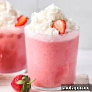 Quick Strawberry Dream Cocktail 6 A glass of pink strawberry milkshake topped with whipped cream and a sliced strawberry, with another drink and a whole strawberry nearby.