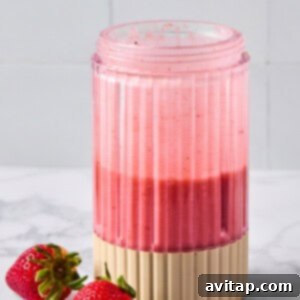 Quick Strawberry Dream Cocktail 7 A pink smoothie in a ribbed glass sits on a marble surface next to two fresh strawberries.