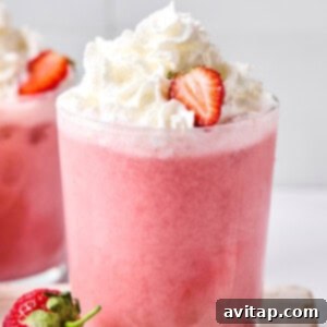 Quick Strawberry Dream Cocktail 9 A glass of pink strawberry smoothie topped with whipped cream and a sliced strawberry, with whole strawberries nearby.