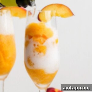 A champagne flute filled with orange sorbet and topped with bubbly drink, garnished with a peach slice on the rim.