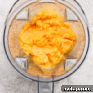 Luscious Frozen Peach Bellini 8 Top-down view of an open blender containing a smooth, orange-yellow mixture on a light textured surface.