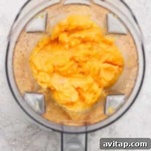 Top-down view of an open blender containing a smooth, orange-yellow mixture on a light textured surface.