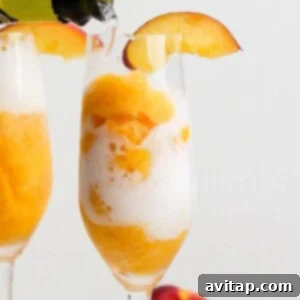 A champagne flute filled with orange sorbet and topped with bubbly drink, garnished with a peach slice on the rim.