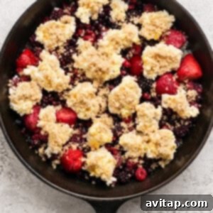 Creamy Protein Berry Cobbler 9 A cast iron skillet filled with mixed berries topped with dollops of crumbly dough and brown sugar, ready for baking.