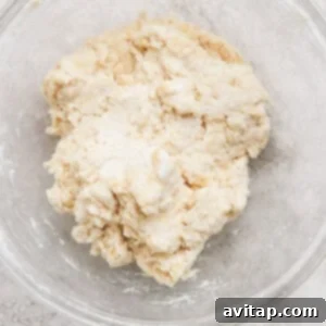 Creamy Protein Berry Cobbler 7 A glass bowl containing a rough, partially-mixed dough on a light-colored surface.