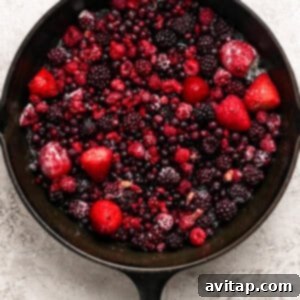 Creamy Protein Berry Cobbler 8 A cast iron skillet filled with a mix of frozen berries, including strawberries, raspberries, blackberries, and blueberries, on a light textured surface.