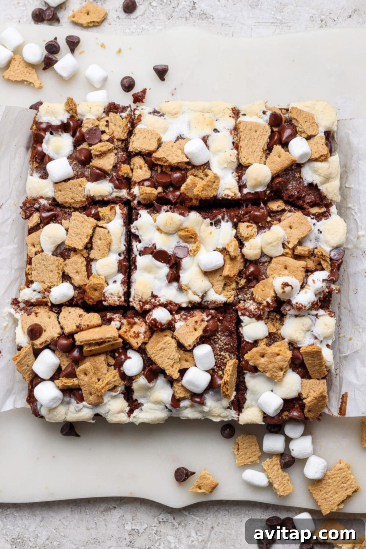 A batch of perfectly cut s'mores bars, adorned with mini marshmallows, graham cracker pieces, and chocolate chips, arranged on parchment paper – a tantalizing display of protein-packed treats.