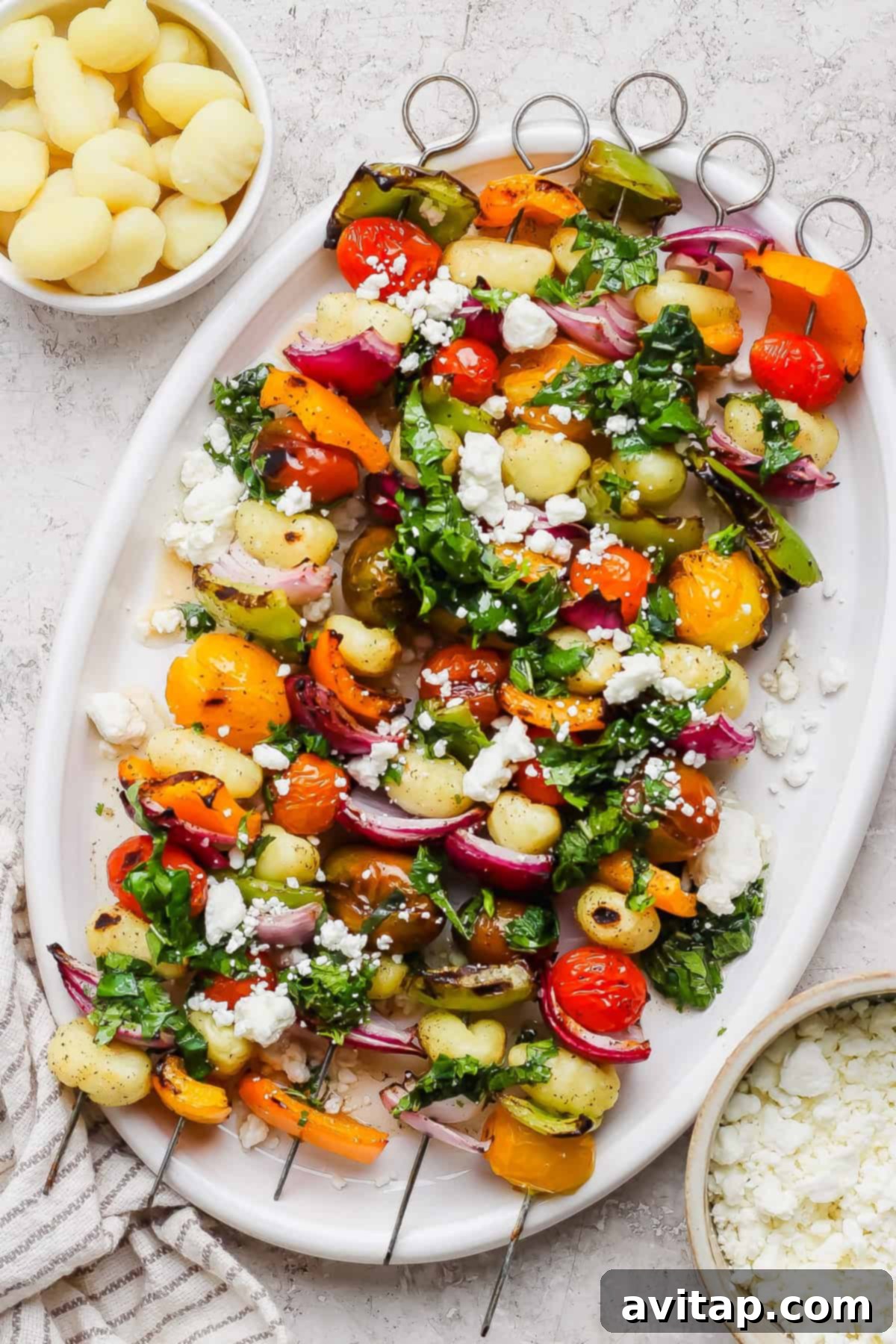 Grilled Rainbow Gnocchi Pops 2 A white platter showcasing colorful grilled gnocchi and vegetable skewers, beautifully topped with fresh chopped herbs and crumbled goat cheese.