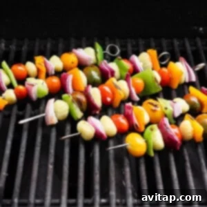 Grilled Rainbow Gnocchi Pops 10 Vegetable skewers with tomatoes, onions, bell peppers, and gnocchi are grilling on a barbecue grate.