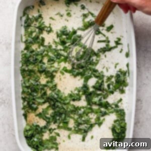 Grilled Rainbow Gnocchi Pops 11 A hand uses a whisk to mix chopped greens and liquid with seasonings in a white rectangular baking dish.