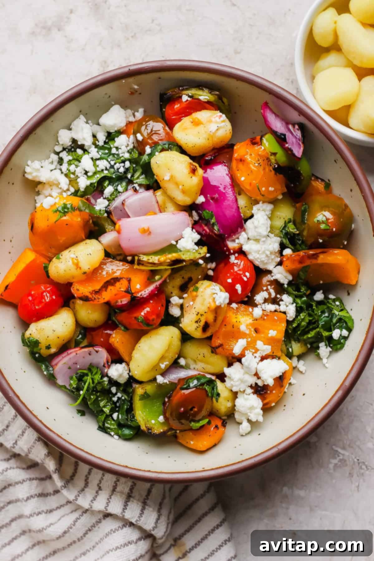 Grilled Rainbow Gnocchi Pops 4 A large bowl filled with a delightful mix of roasted gnocchi, colorful bell peppers, red onion, cherry tomatoes, fresh leafy greens, and crumbled feta cheese, with a smaller bowl of cooked gnocchi on the side.
