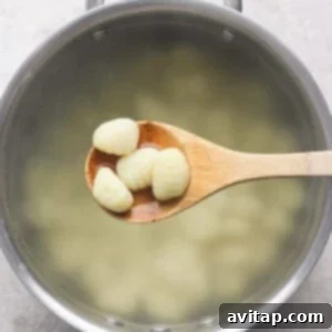 Grilled Rainbow Gnocchi Pops 6 A wooden spoon holds several pieces of gnocchi over a pot of boiling water.