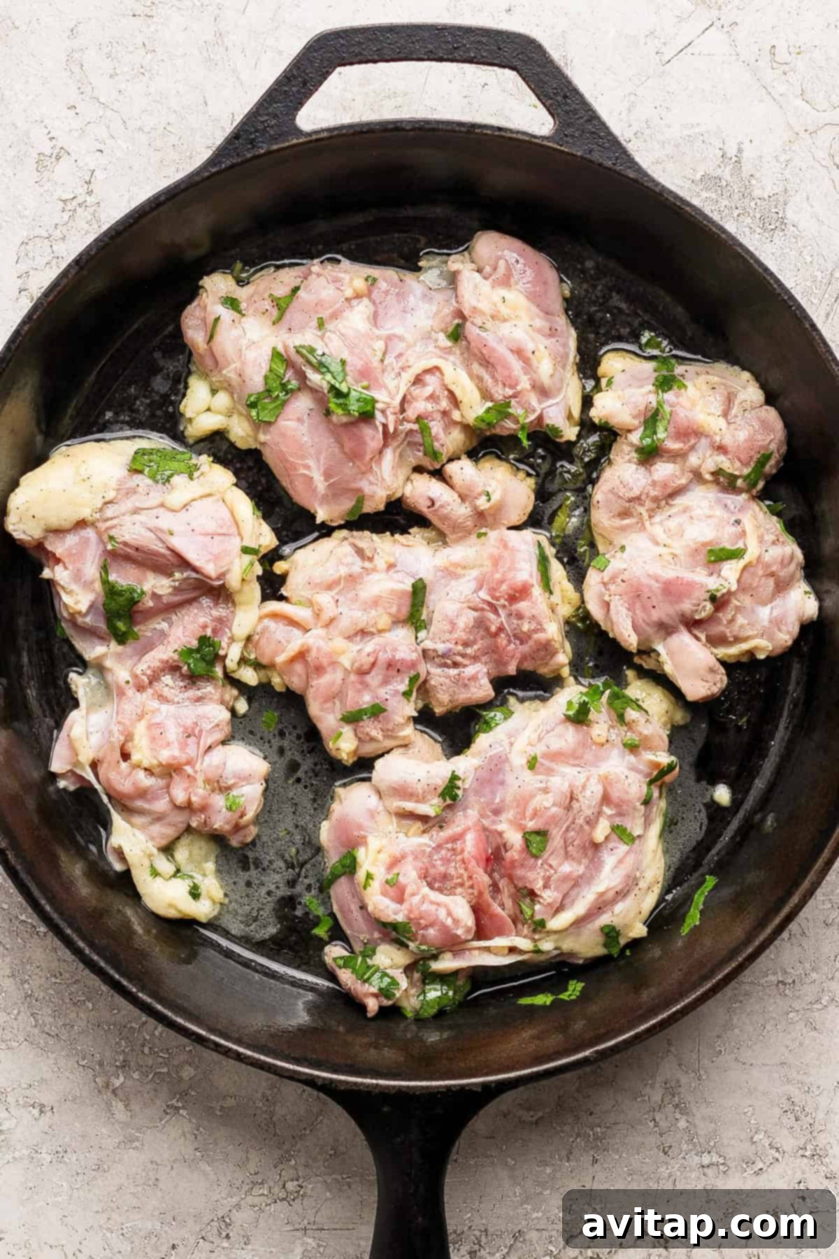 Raw marinated chicken pieces generously coated with fresh herbs and spices, nestled in a sleek black cast iron skillet on a light countertop, perfectly prepped for cooking and a healthy meal.