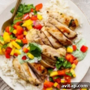 A chicken meal prep plate featuring grilled chicken slices on white rice, topped with diced mango, red bell pepper, cilantro, and a drizzle of green sauce, served with a fork on the side.