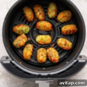 Twelve cooked vegetable tots arranged neatly in a single layer inside the basket of an air fryer, looking golden and crispy.