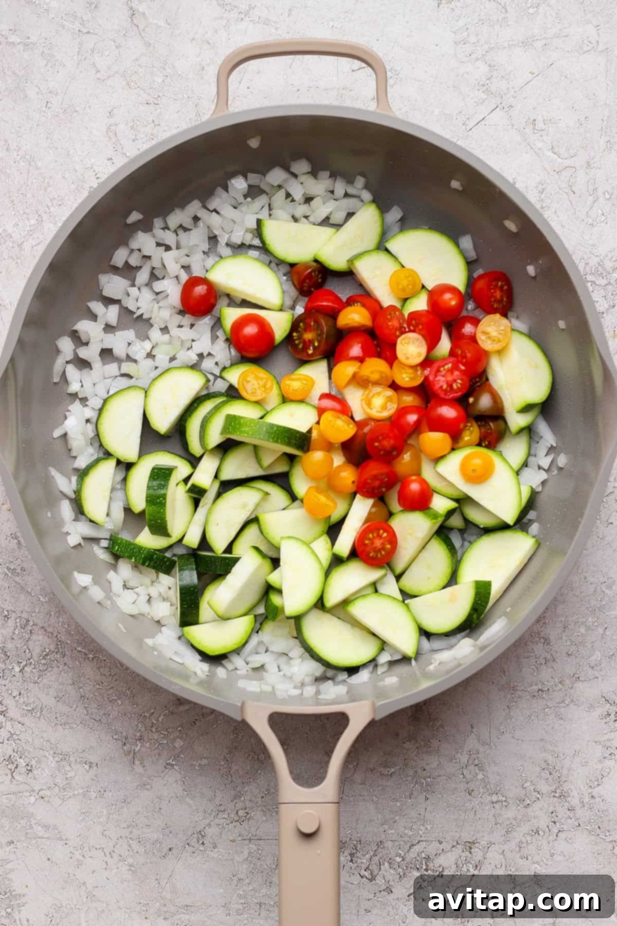 Chopped onions, sliced zucchini, and halved cherry tomatoes sizzling in a frying pan with olive oil.