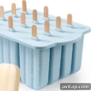 A blue silicone popsicle mold with twelve slots and wooden sticks, displayed next to a single creamy protein fudgesicle.