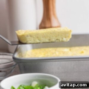 A spatula gently lifts a rectangular slice of perfectly baked egg from its metal pan, with a small bowl of finely chopped green onions visible in the soft foreground, ready for garnish.