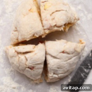 Round ball of uncooked dough cut into four equal pieces on floured parchment paper, with a knife placed beside it.