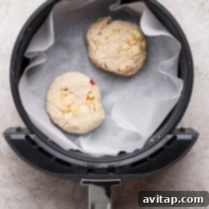 Two unbaked dough rounds with visible chunks, placed on parchment paper inside an air fryer basket.