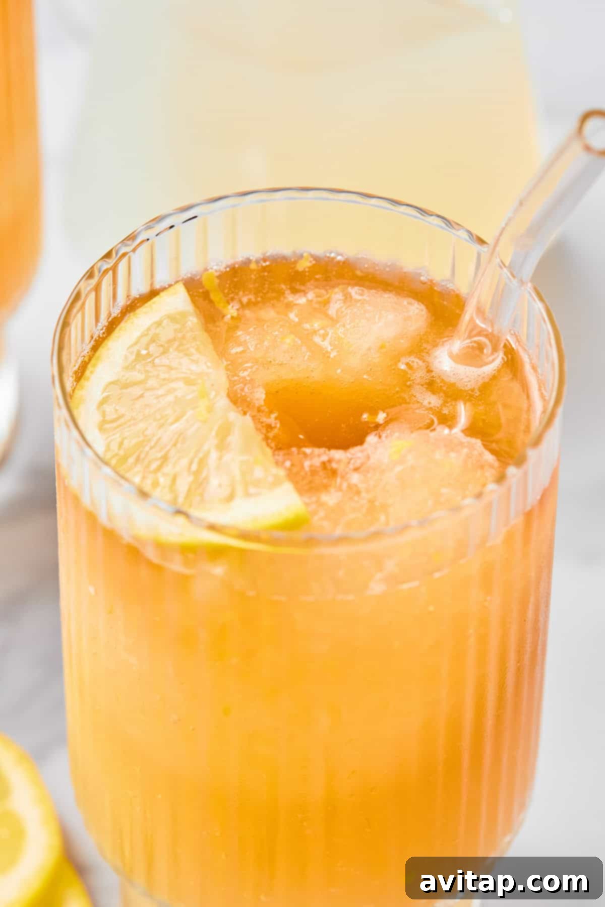 A close-up shot of an iced orange beverage in a beautifully ribbed glass, complete with a clear straw and a vibrant lemon slice garnish.