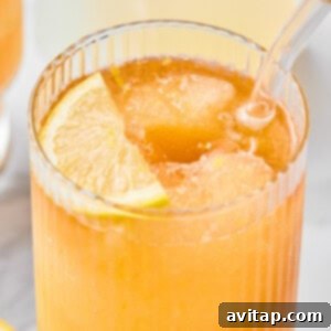 A close-up of an iced orange drink in a ribbed glass with a clear straw and a lemon slice garnish.