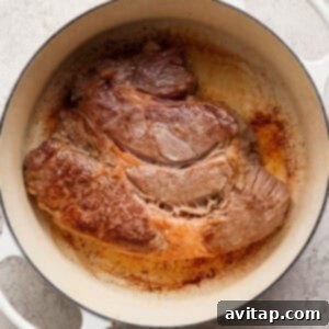 OLIPOP Infused Chuck Roast 10 A large piece of perfectly seared beef sits in a white Dutch oven, exhibiting a rich, brown crust on a light-colored surface, ready for the next cooking stage.