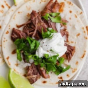 A delicious flour tortilla taco, topped with tender shredded beef, fresh chopped onions, vibrant cilantro, and a dollop of creamy sour cream, served alongside a bright lime wedge.
