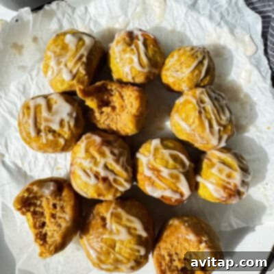 A dozen small, round cakes with white icing drizzle, some with bites taken out, are arranged on crumpled parchment paper under natural light.