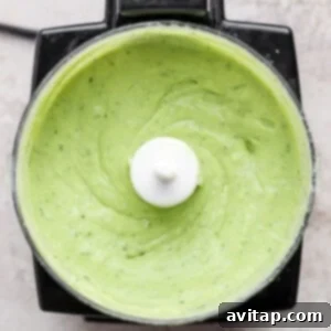 Top-down view of a food processor blending ingredients into a smooth, vibrant green avocado crema, ready to be served with the tacos.